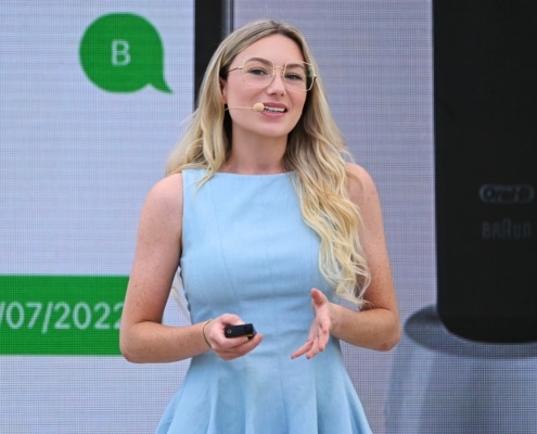 Photo of World Ostomy Day Champion Keely Cat-Wells a white woman with blond hair and a blue dress speaking at a professional conference.